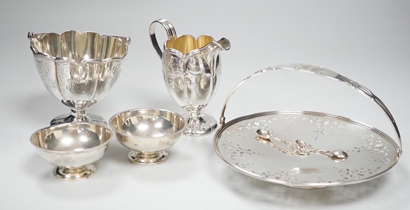 A sterling sugar basket, diameter 9.9cm, a sterling shallow basket dish, sterling cream jug and pair of sterling salts with spoons, 20.6oz.